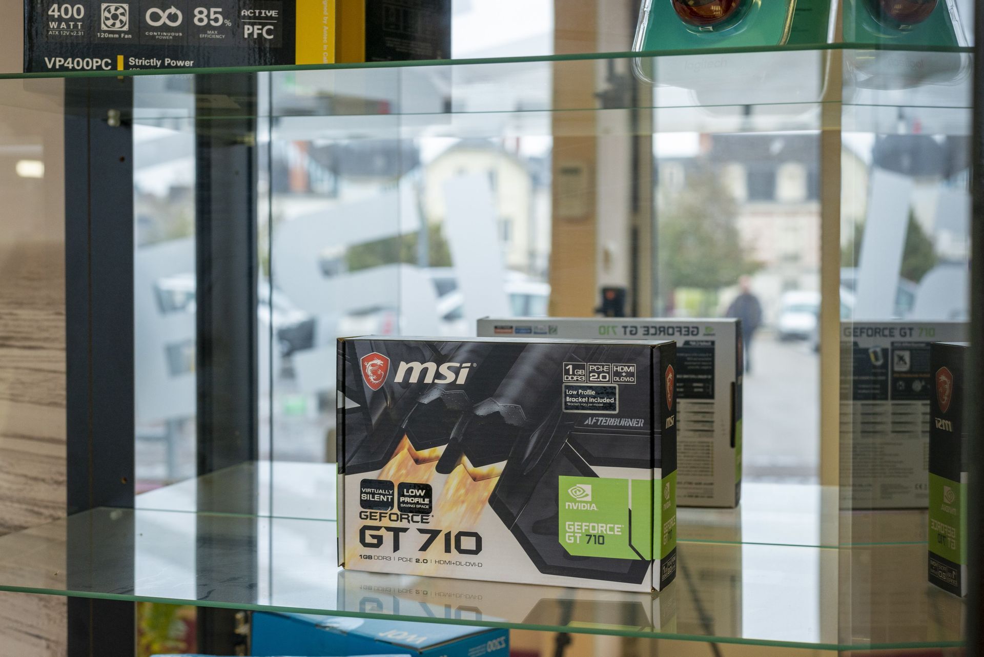 Boîte de carte graphique MSI exposée dans une vitrine, avec des reflets de la devanture en arrière-plan.