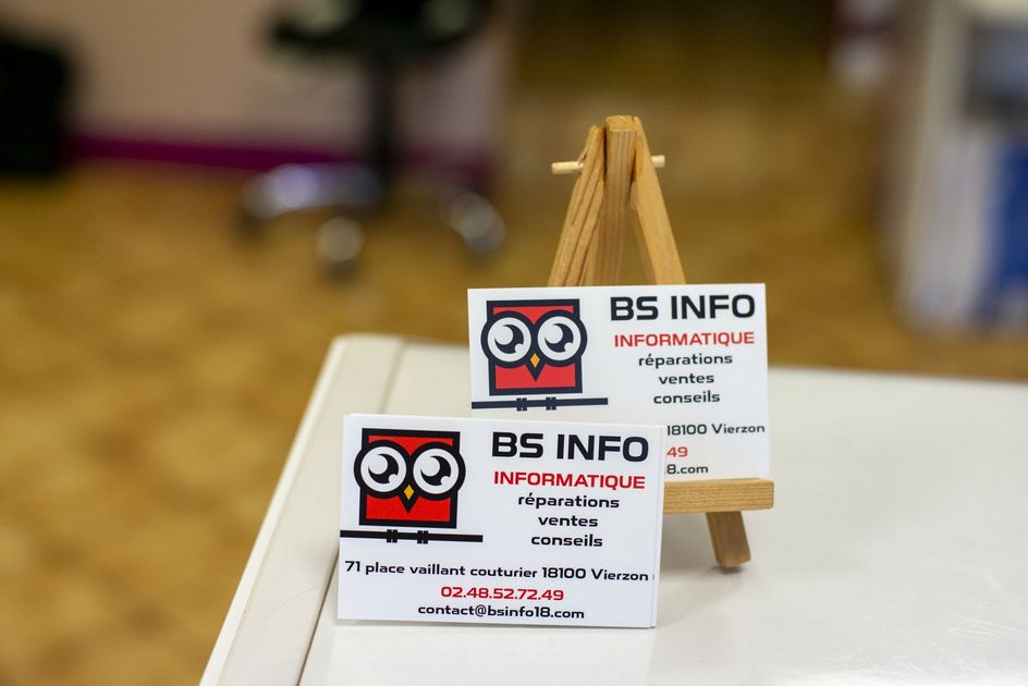 Deux cartes de visite BS Info présentées sur un petit chevalet en bois posé sur une table blanche.