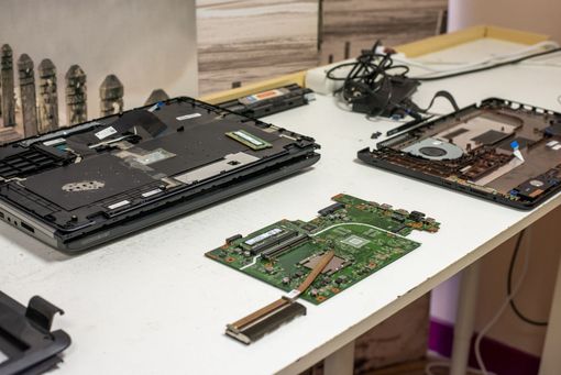 Composants d’ordinateur portable démonté disposés sur un établi, notamment une base noire, des cartes électroniques et des câbles.