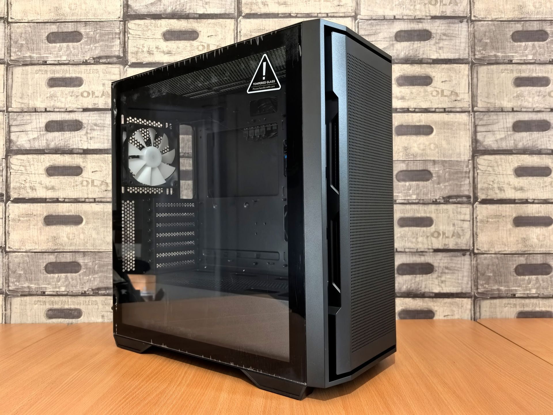 Tour d’ordinateur de bureau noire avec un panneau latéral en verre, posée sur un bureau en bois contre un mur de briques