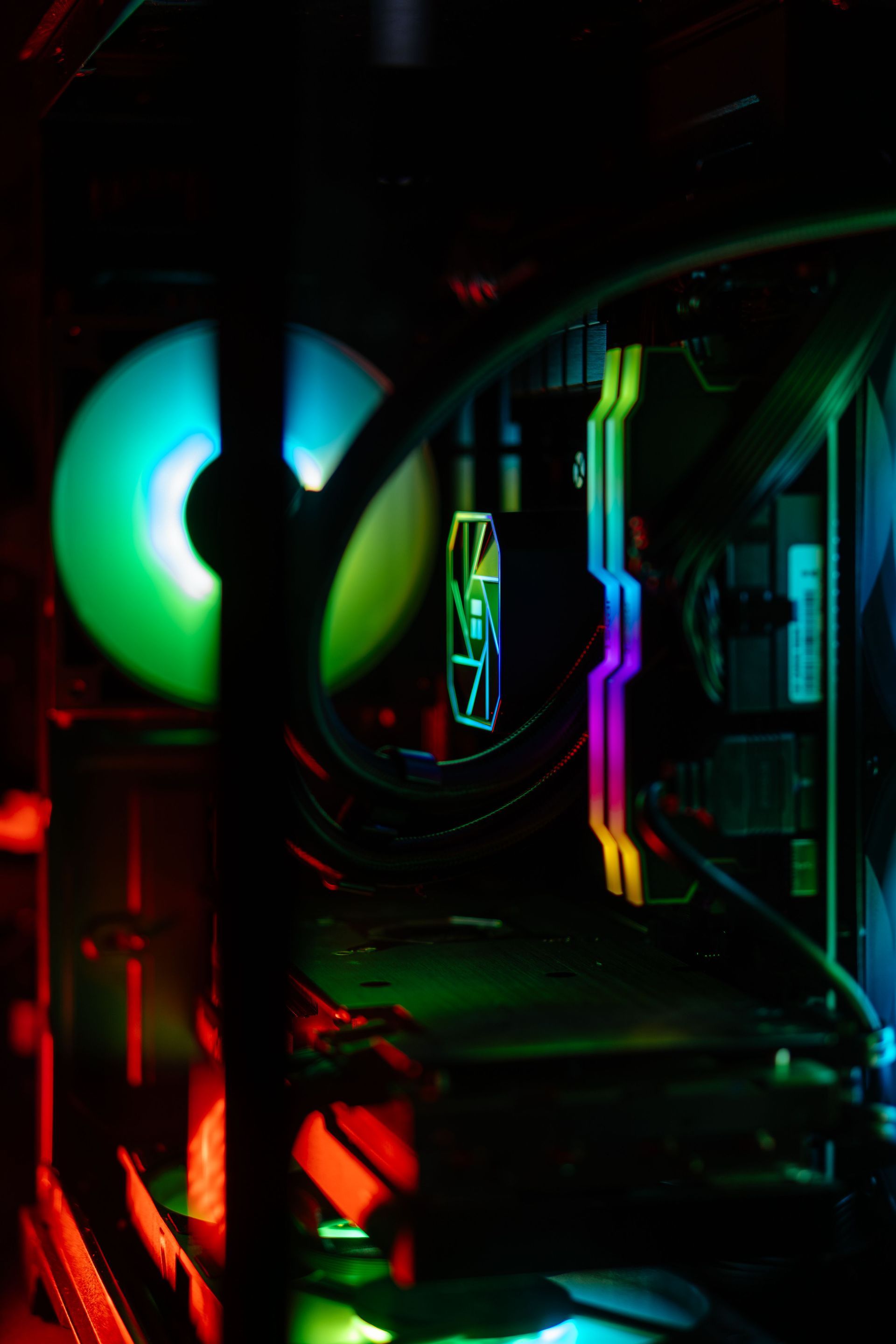 Intérieur d’un PC de jeu éclairé par des LED RGB, avec ventilateur lumineux et câbles arc-en-ciel dans un boîtier sombre