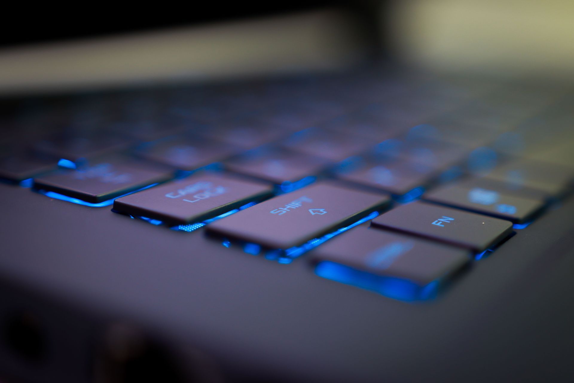 Gros plan sur le clavier d’un ordinateur portable aux touches rétroéclairées en bleu, dans une pièce tamisée