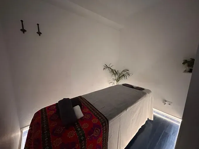 Sala de spa minimalista con camilla de masaje, paredes blancas e iluminación ambiental suave.