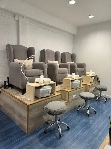 Spa de pedicura con sillones de masaje grises, reposapiés y taburetes sobre un suelo alfombrado de color azul.