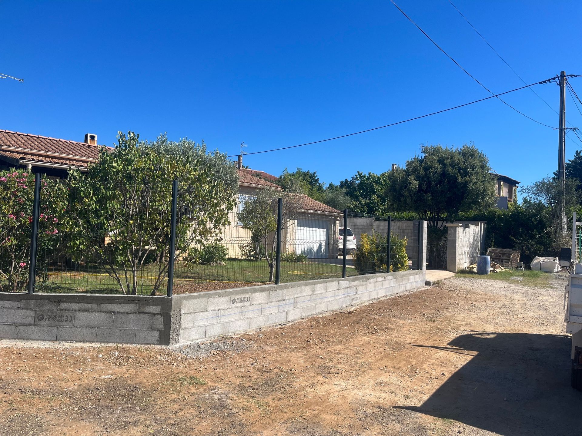 Un mur de clôture avec un soubassement en parpaings et des panneaux rigides.