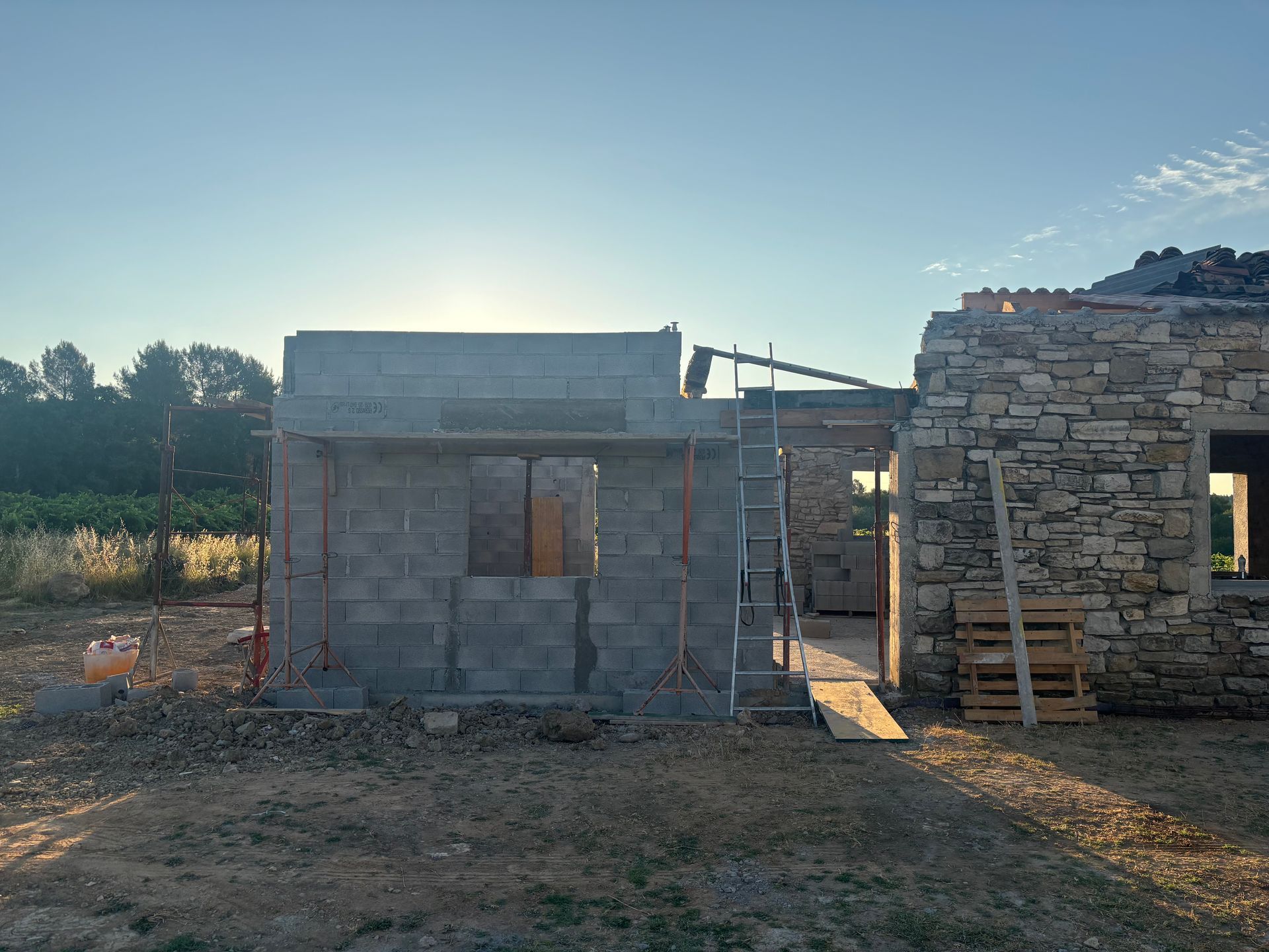 Construction d'une extension de maison en parpaings le long d'une maison en pierre.