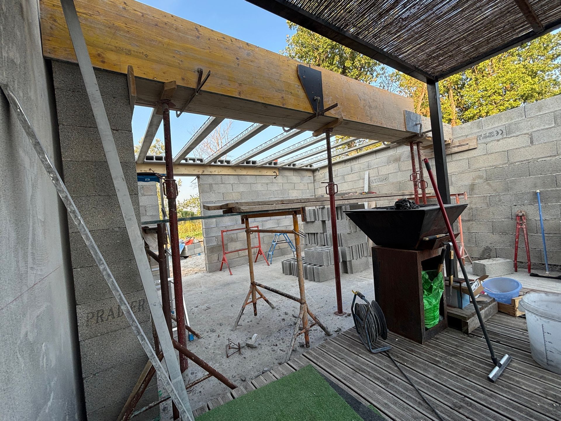 Zone de construction en parpaings avec des poutres en bois et du matériel de chantier.