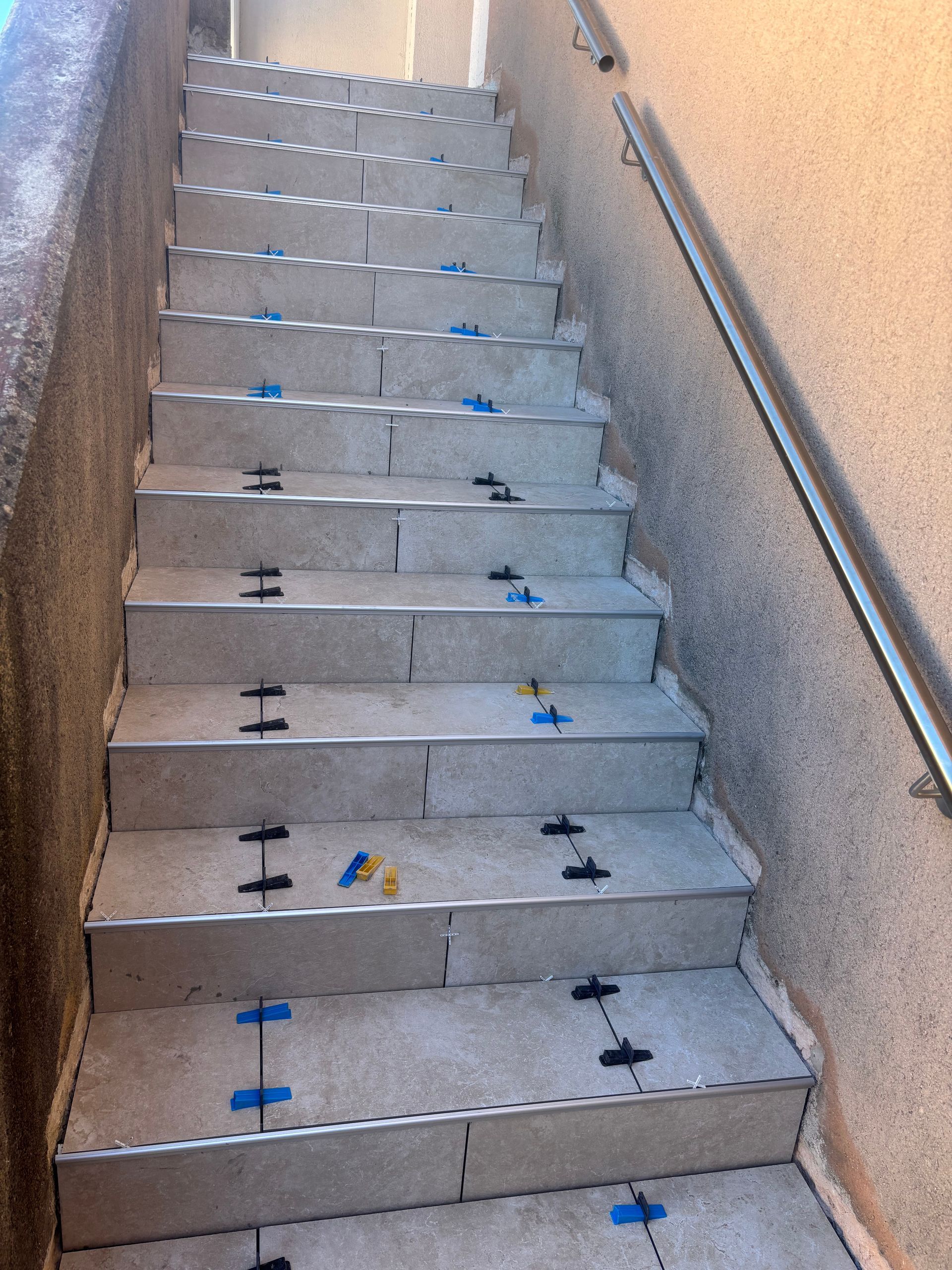 Des escaliers carrelés avec des rampes métailliques.