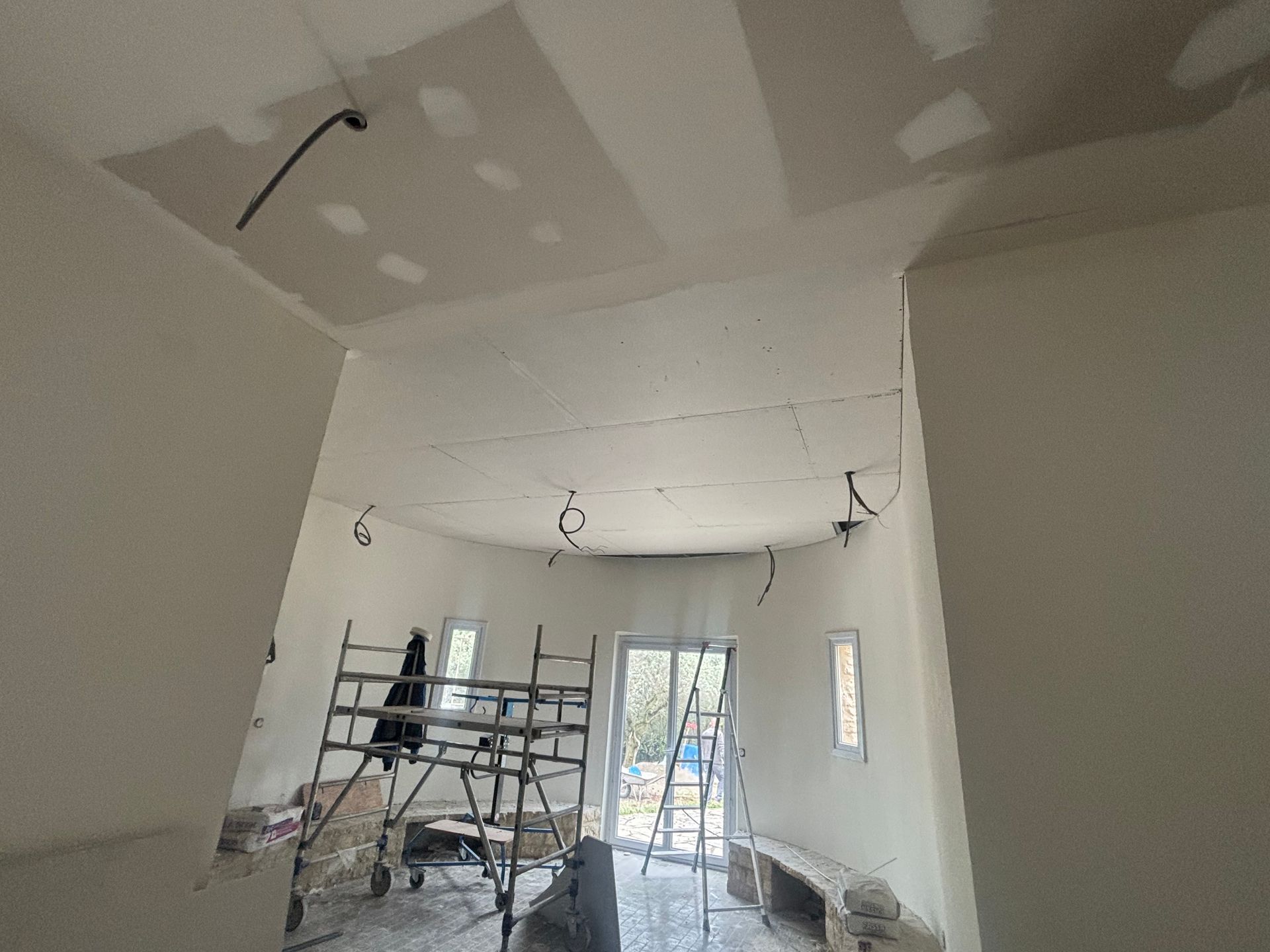 Un échafaudage avec des gaines électriques qui sortent d'un plafond en plaques de plâtre.