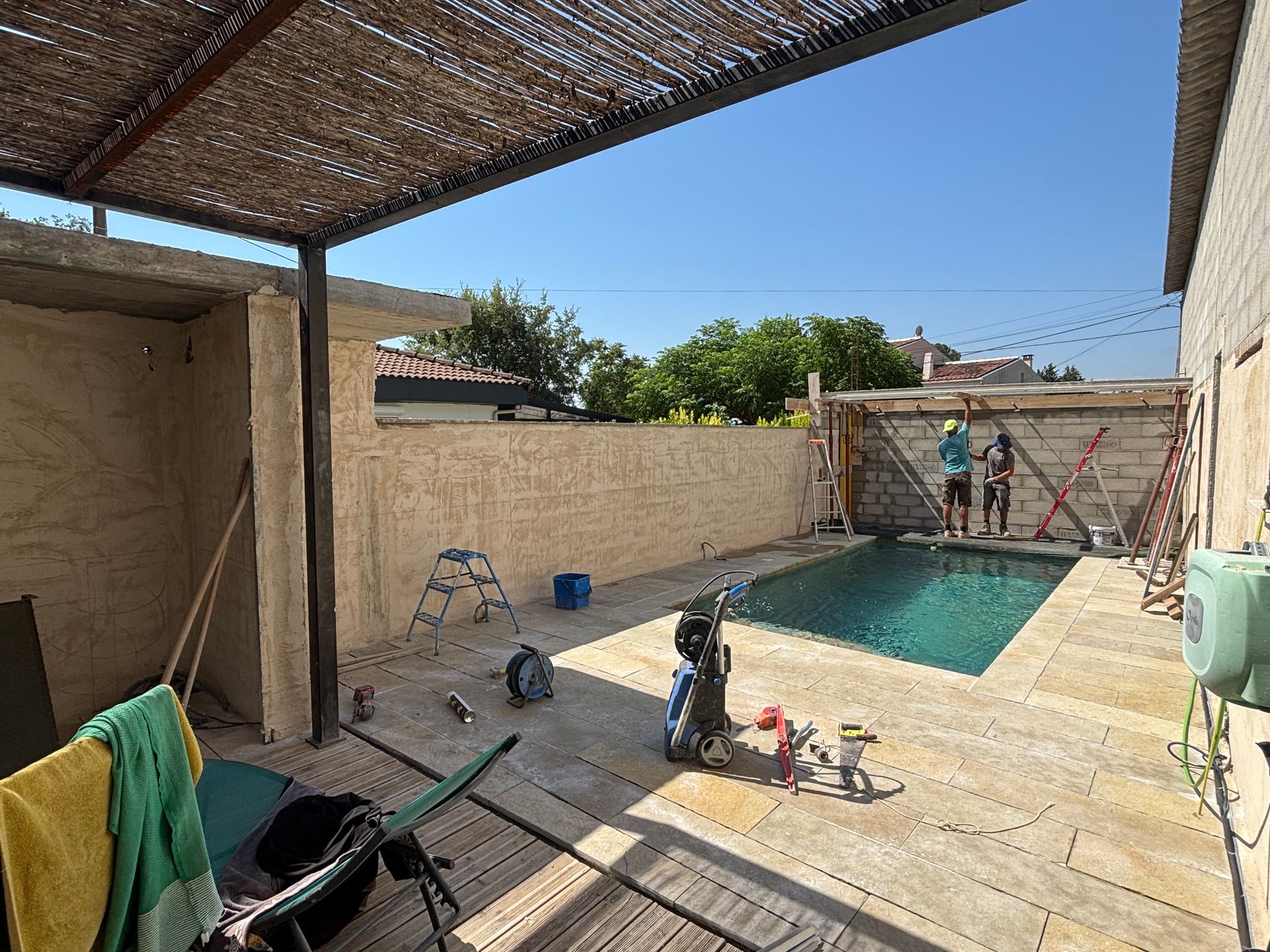 Une terrasse avec une piscine et des ouvriers en train de ravaler un mur de clôture.
