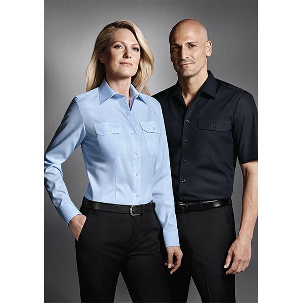 Frau im hellblauen Hemd, Mann im schwarzen Hemd, beide in schwarzen Hosen, posieren vor einem grauen Hintergrund.