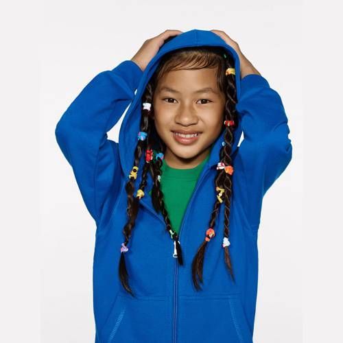 Mädchen in blauem Kapuzenpullover, lächelnd, hält Kapuze hoch, geflochtenes Haar mit bunten Perlen.