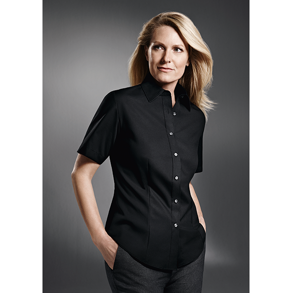 Frau trägt ein schwarzes kurzärmeliges Button-Down-Hemd, Hände in den Taschen.