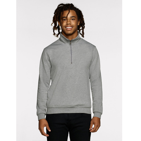 Mann im grauen Pullover mit Viertelreißverschluss, schwarze Hose, lächelnd. Hellgrauer Hintergrund.