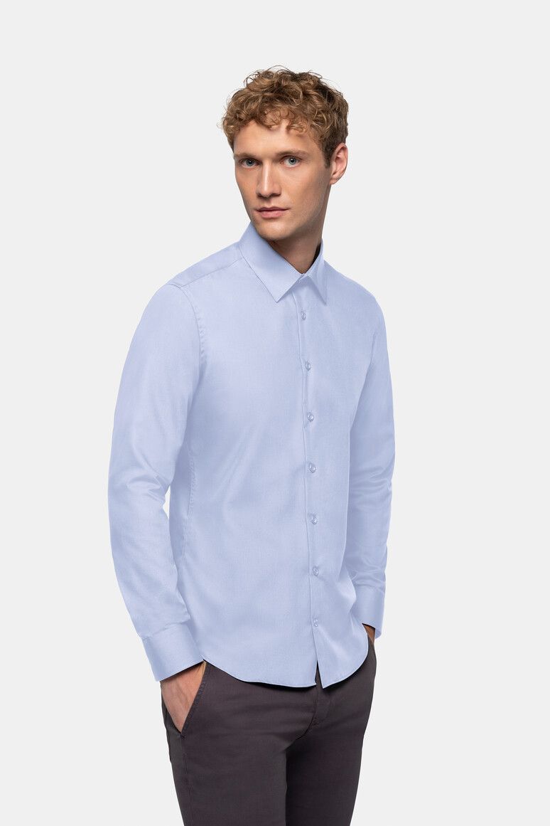 Mann trägt ein hellblaues Hemd und graue Hosen, die Hände in den Taschen.