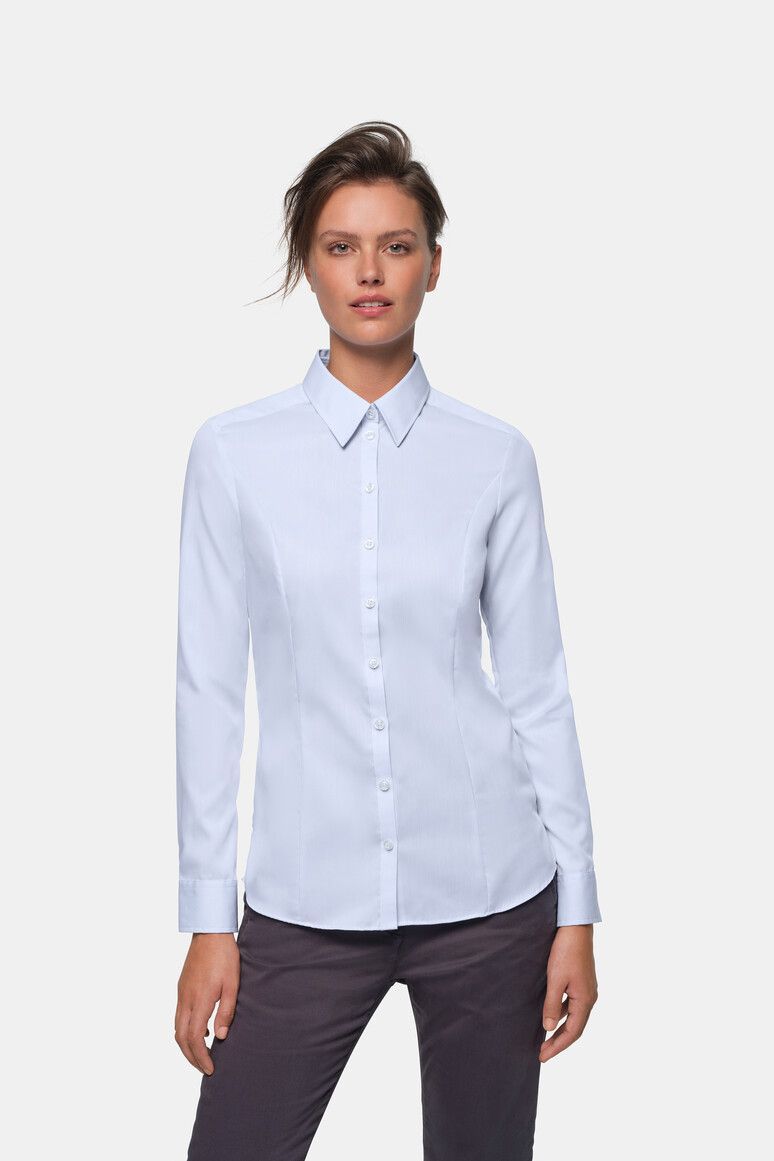 Frau in hellblauem Button-Down-Hemd und dunkler Hose, stehend und nach vorne blickend.
