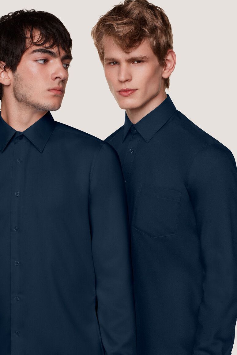 Zwei Männer in marineblauen Hemden, die vor einem neutralen Hintergrund in entgegengesetzte Richtungen blicken.