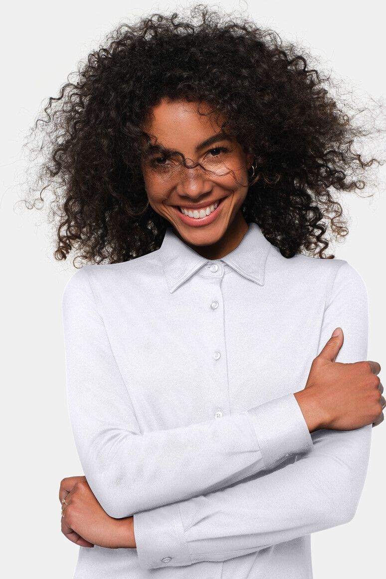 Frau mit lockigem dunklem Haar, trägt ein weißes Button-Down-Hemd und lächelt.