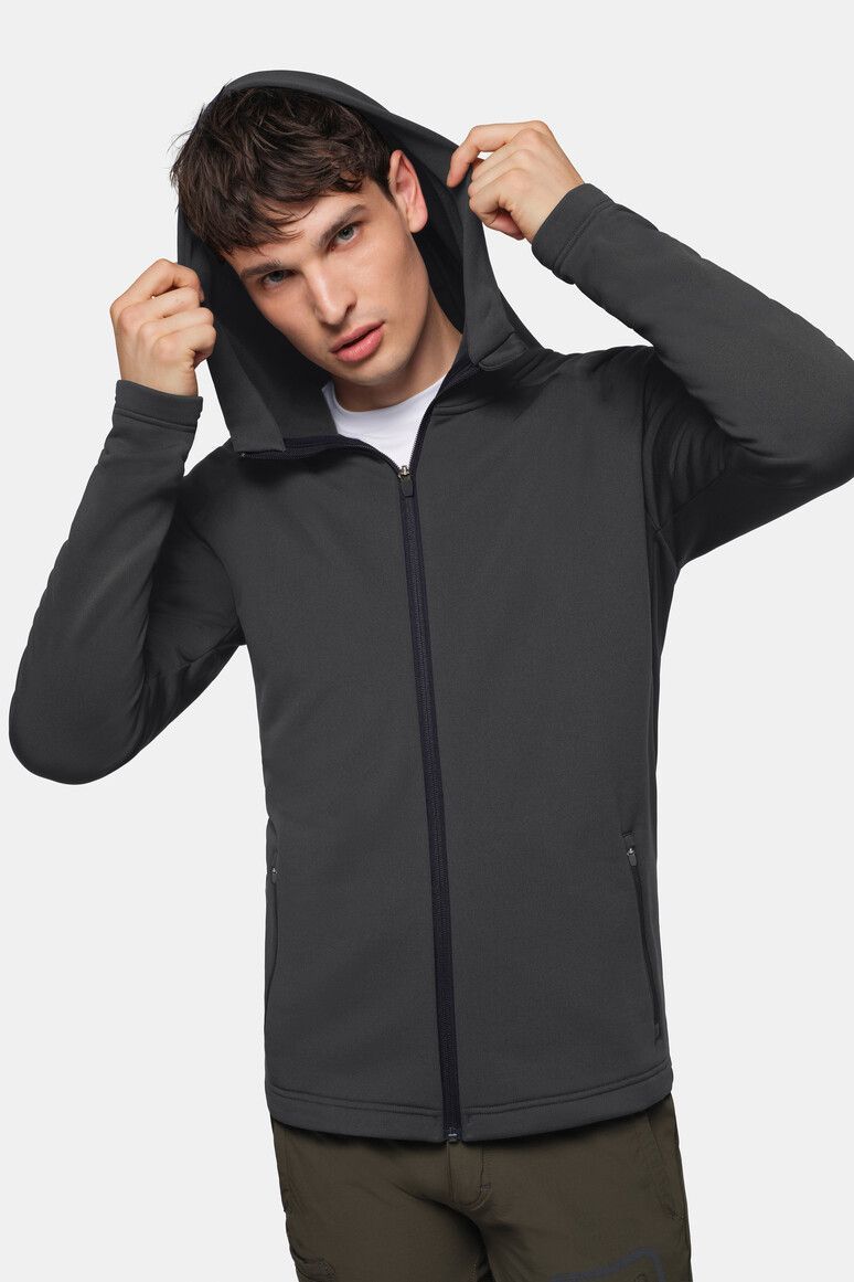 Mann in grauer Kapuzenjacke, zieht die Kapuze hoch und blickt zum Betrachter.