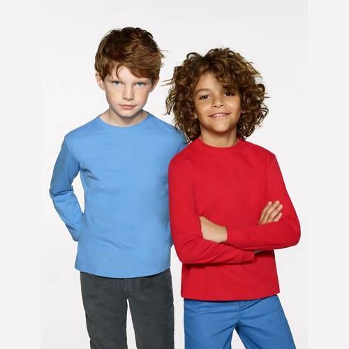 Zwei Jungen in langärmeligen Hemden: einer blau, einer rot. Der Junge im blauen Hemd steht mit den Händen in den Taschen. Der Junge im roten Hemd hat die Arme verschränkt.