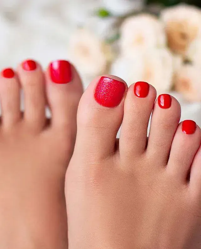 Un primer plano de los pies de una mujer con uñas rojas.