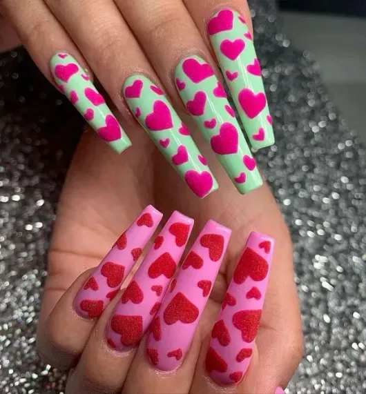 Un primer plano de las uñas de una mujer con corazones rosados ​​y verdes en ellas.