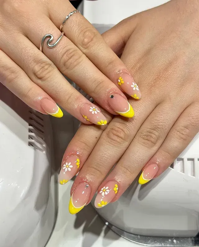 Un primer plano de las uñas de una mujer con una manicura francesa amarilla.