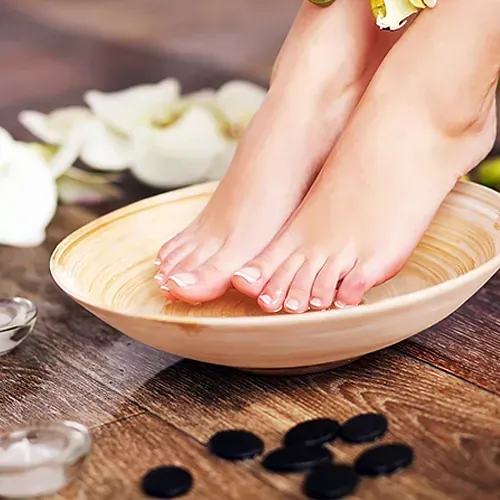 Los pies de una mujer están en un recipiente sobre una mesa de madera.