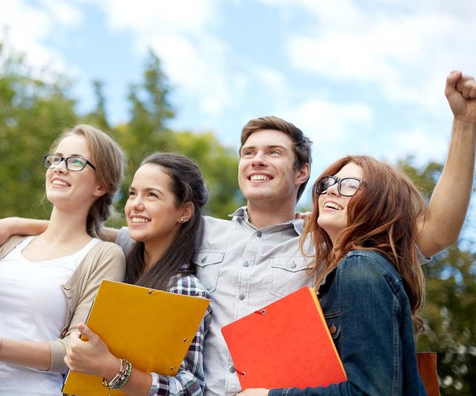 Cuatro estudiantes sonrientes al aire libre, sosteniendo cuadernos coloridos y levantando el puño en señal de celebración.