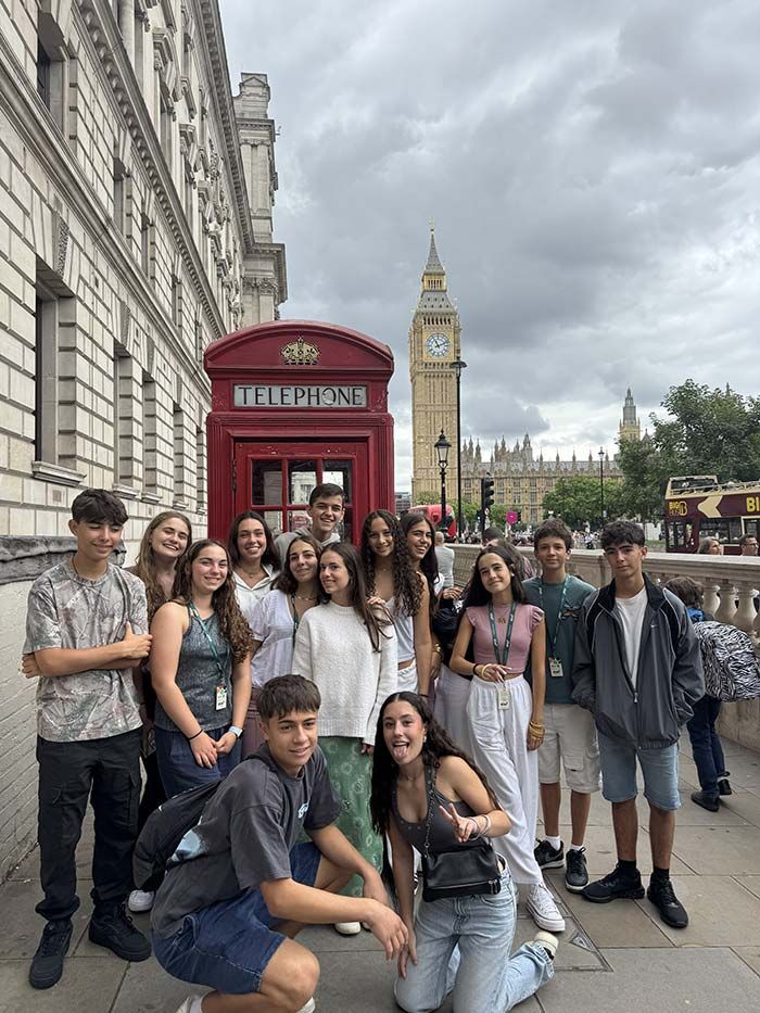 Grupo de turistas posando junto a una cabina telefónica roja en una calle de Londres, con el Big Ben de fondo.
