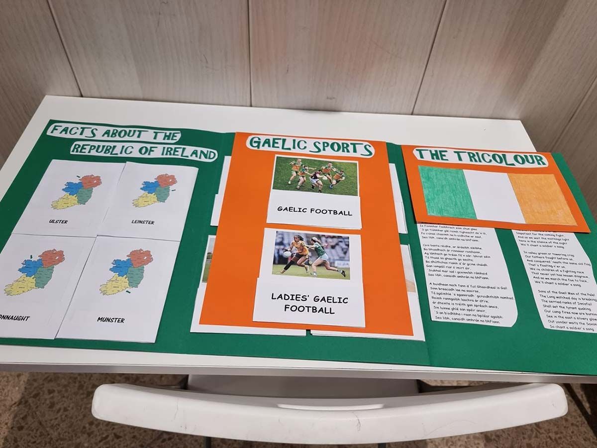 Tres carteles de aula con bordes naranjas sobre un mantel verde; uno de ellos se titula "Deportes Verdes" e incluye notas y dibujos.