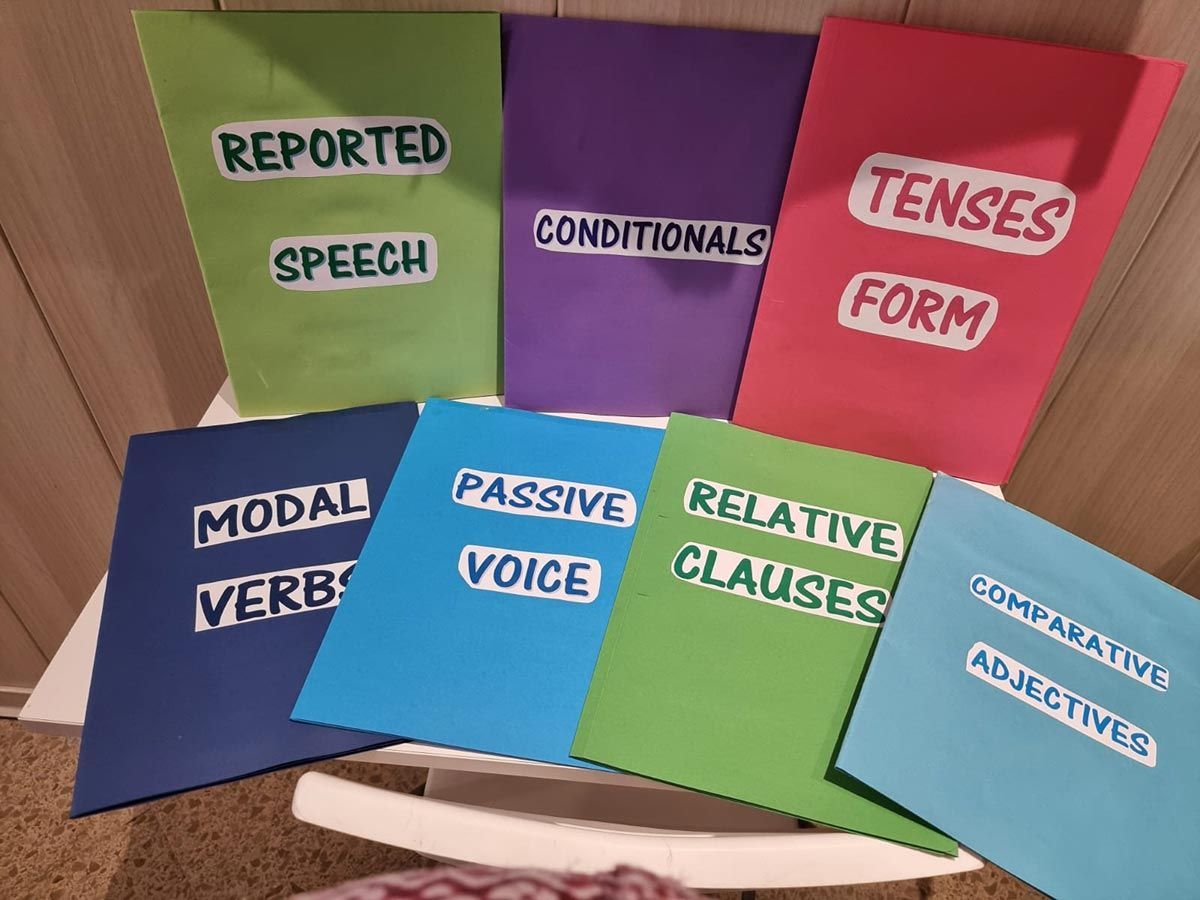 Tarjetas coloridas con temas gramaticales sobre un suelo de madera, etiquetadas con las siguientes palabras: discurso, condicionales, tiempos verbales, verbos modales, voz pasiva, oraciones de relativo, adjetivos.