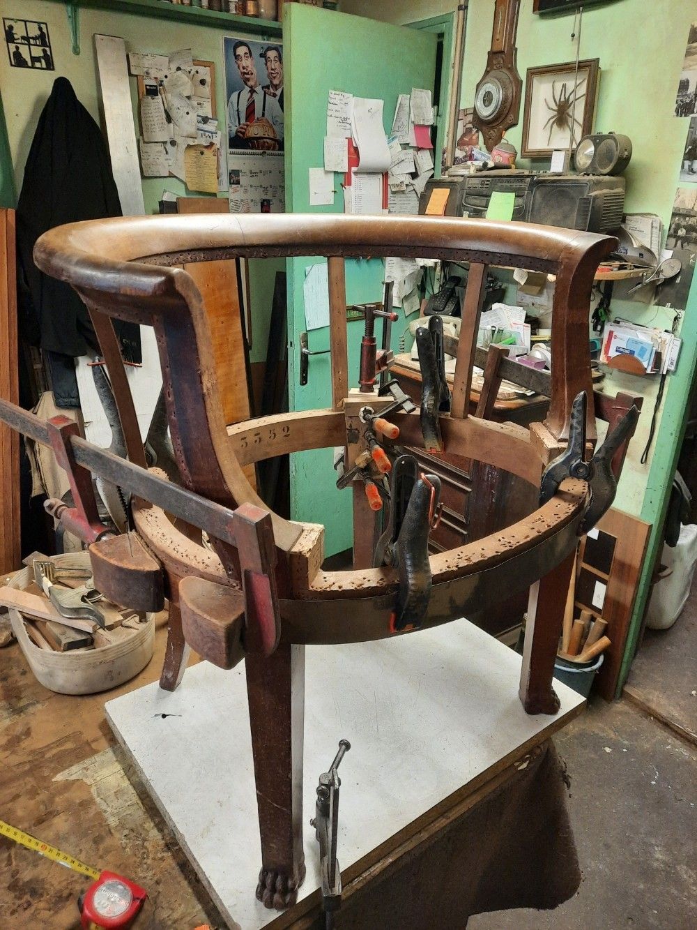 Dans un atelier, une structure de chaise en bois est maintenue par plusieurs serre-joints lors d'une réparation sur un établi.