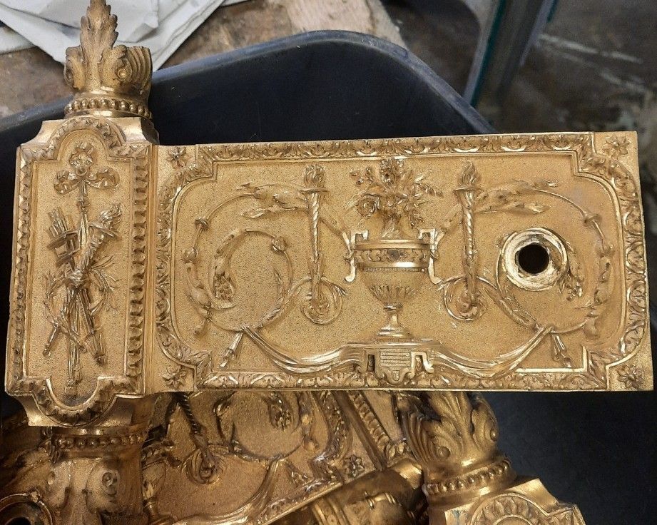 Une serrure ornée de couleur or, avec des détails floraux et de vases, peut-être une façade de tiroir.