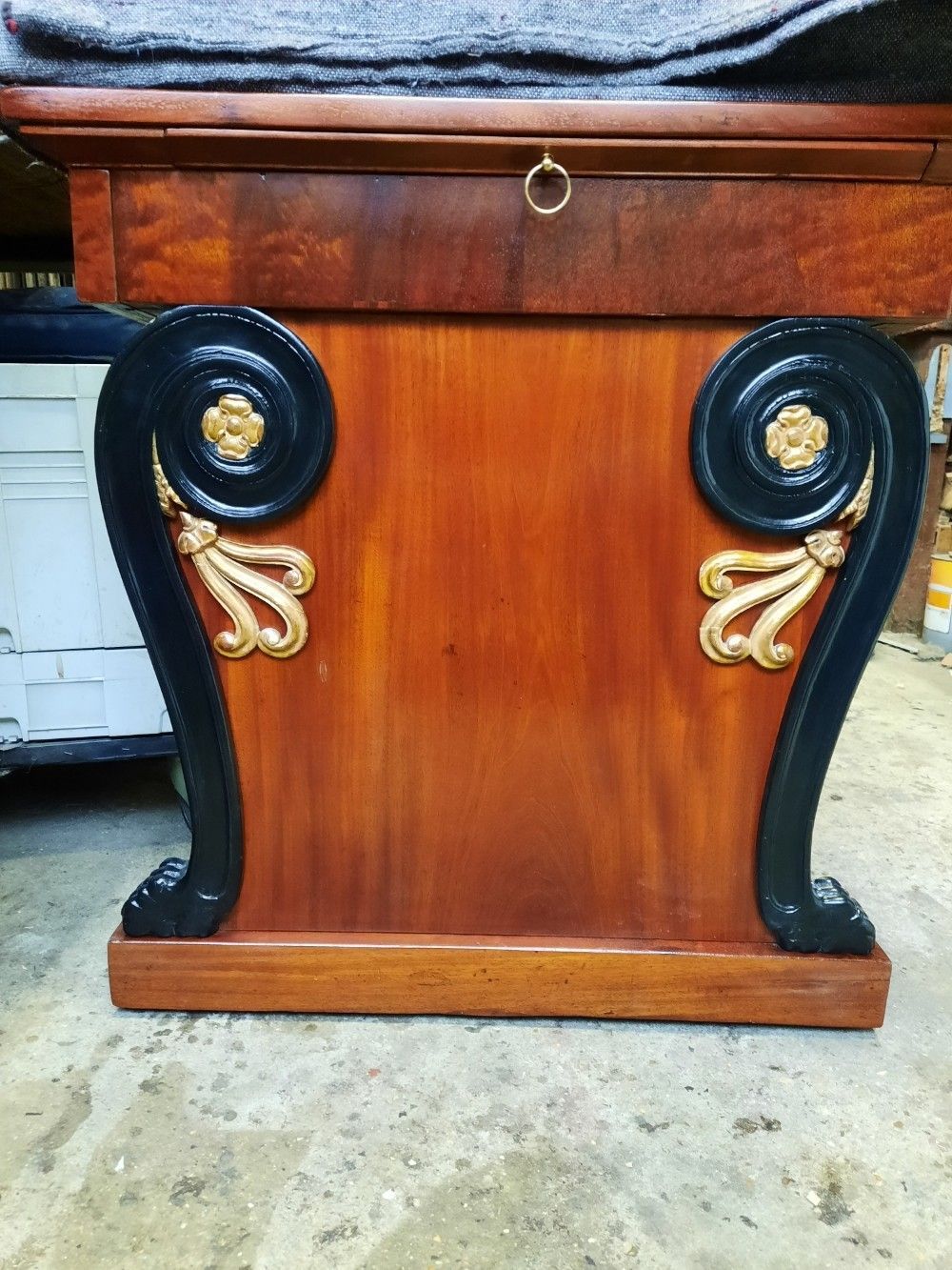 Un pied de table en bois orné de volutes noires rehaussées de dorures sur les deux faces, sur fond uni.