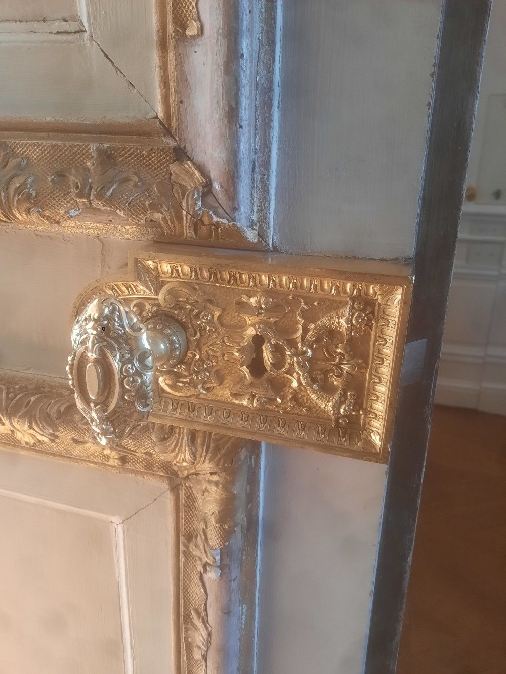 Serrure de porte dorée ornée sur une porte blanche avec garniture dorée.