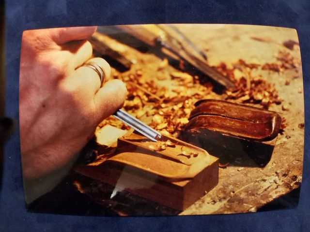 Gros plan sur des mains utilisant un ciseau à métaux pour sculpter des détails complexes dans un petit morceau de bois brun.