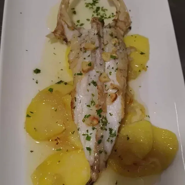 Un plato blanco cubierto con un trozo de pescado y patatas.