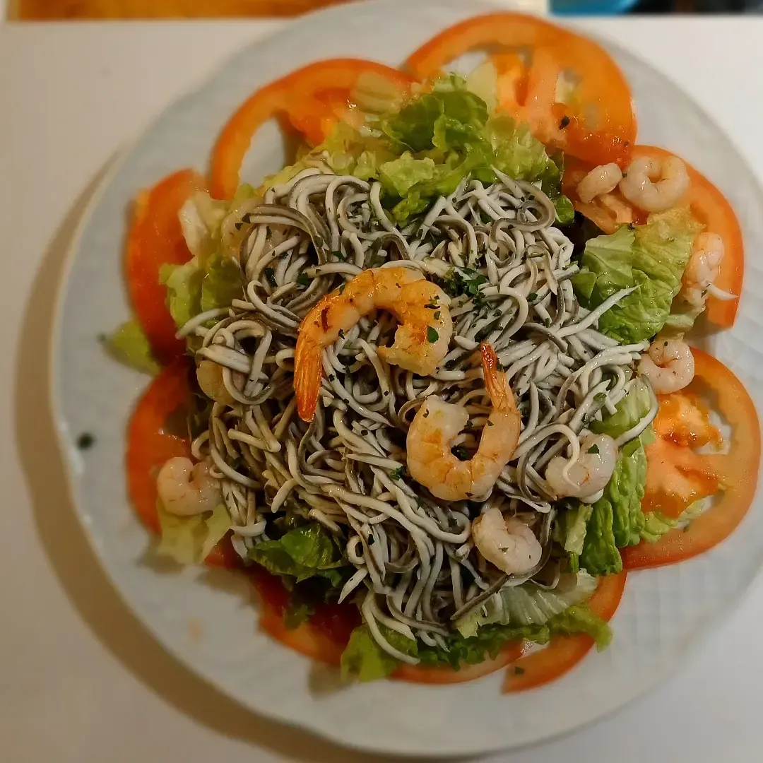 Un plato blanco cubierto con fideos, camarones y tomates.