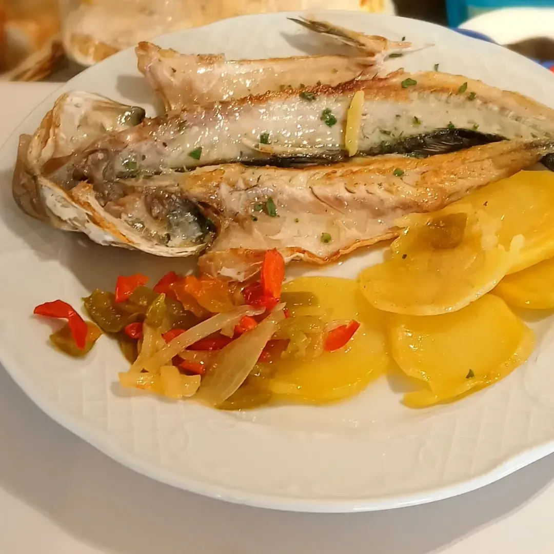 Un plato blanco cubierto con pescado y patatas sobre una mesa.