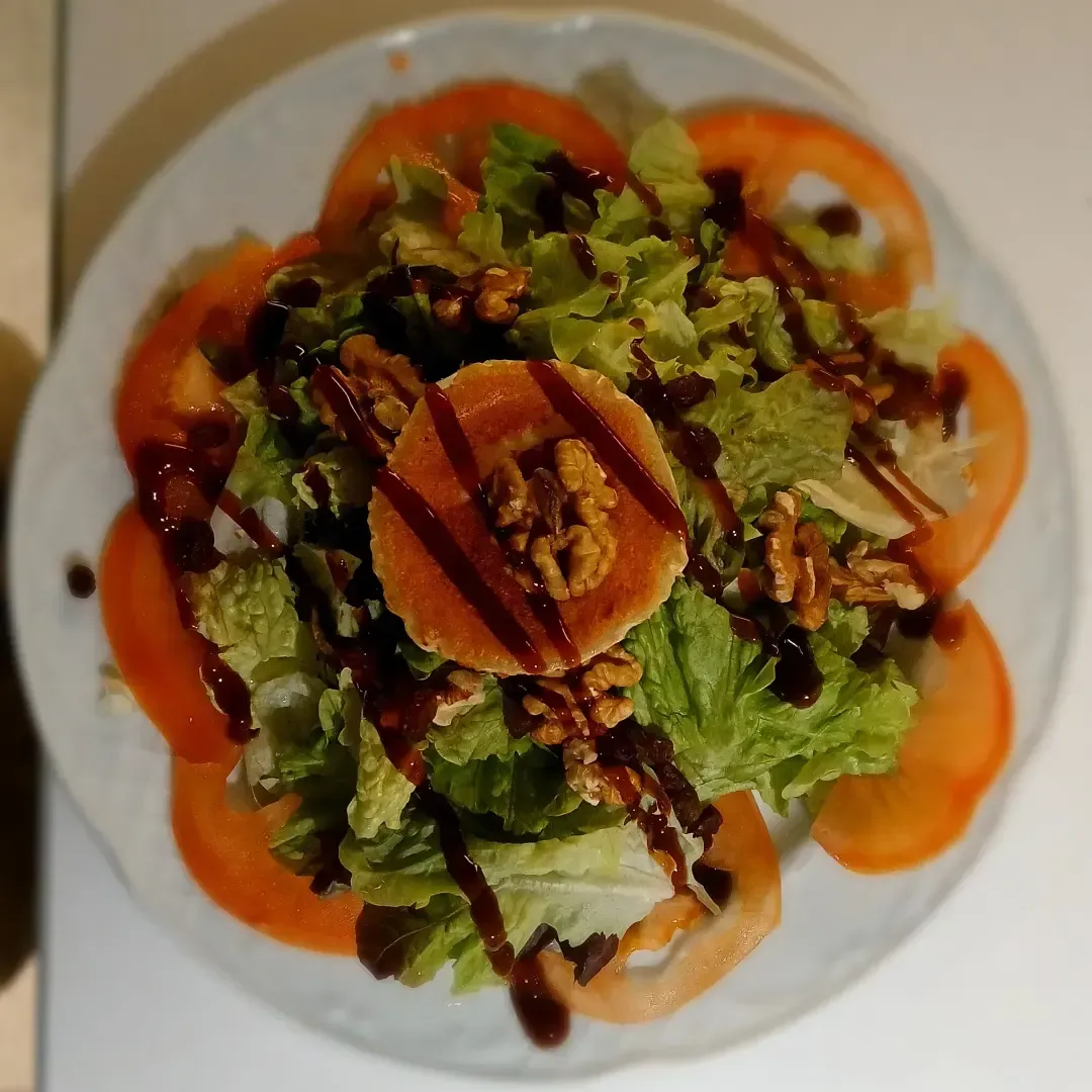 Una ensalada con lechuga, tomates y nueces en un plato blanco.