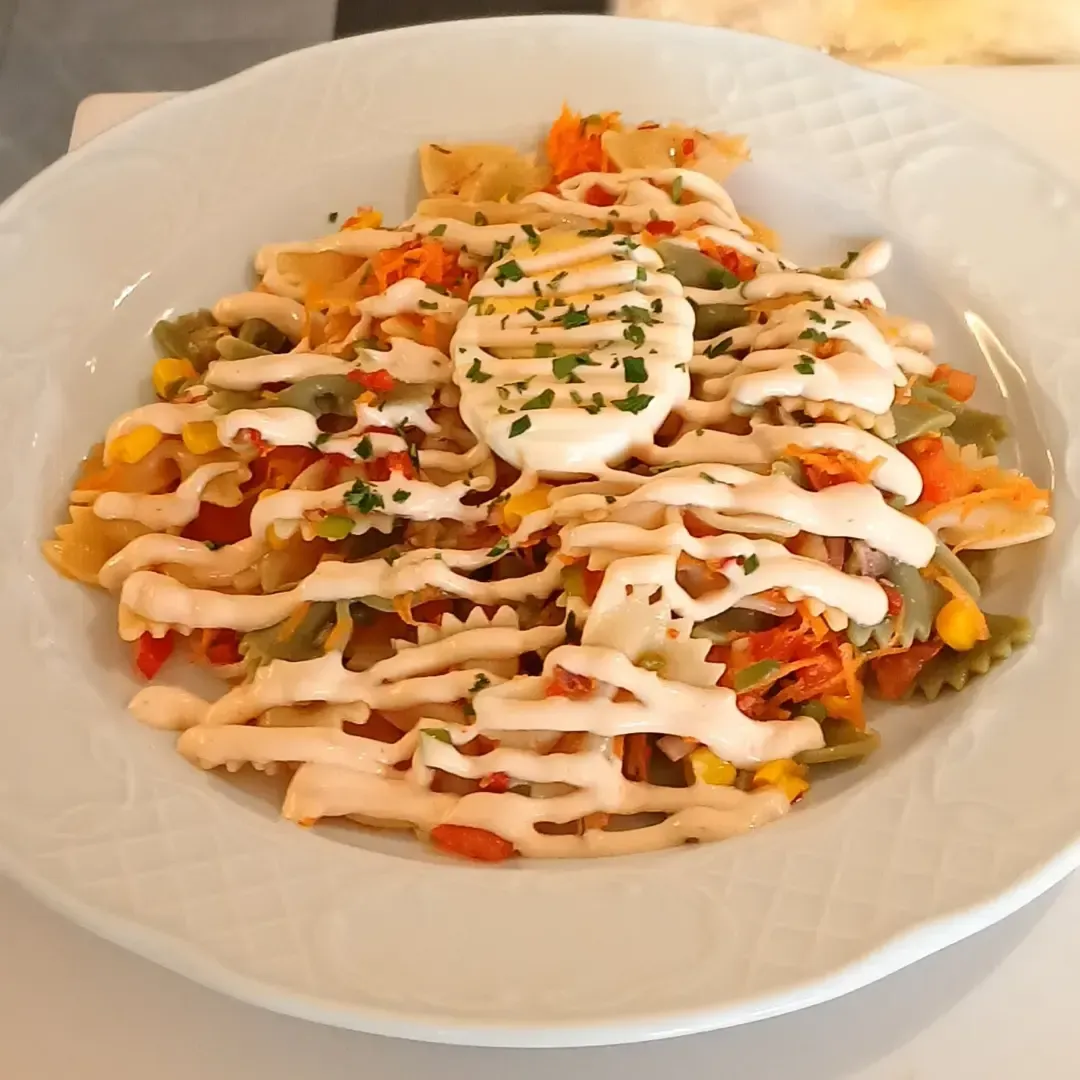 Un plato blanco cubierto con pasta, verduras y mayonesa.