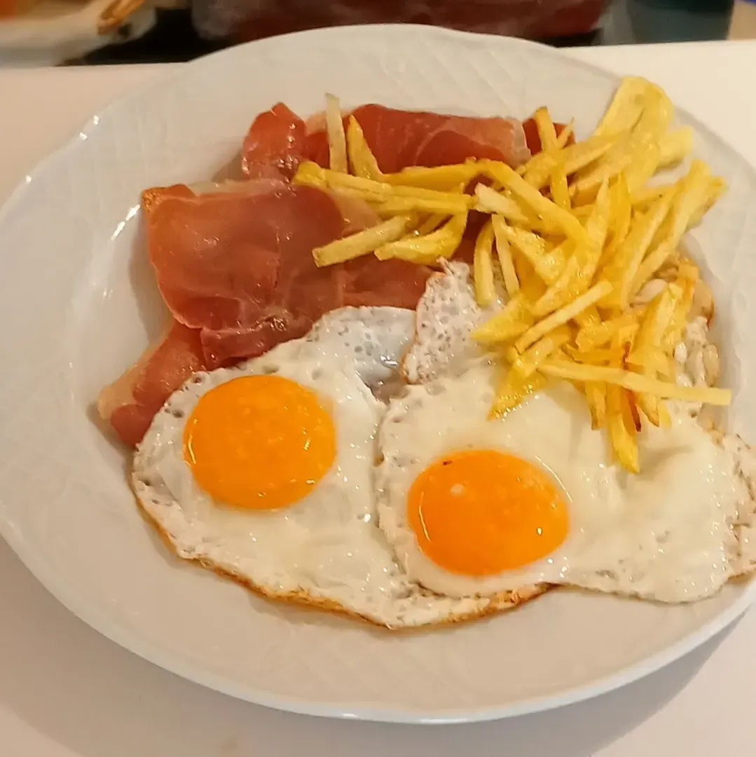 Un plato blanco cubierto con huevos fritos y papas fritas.