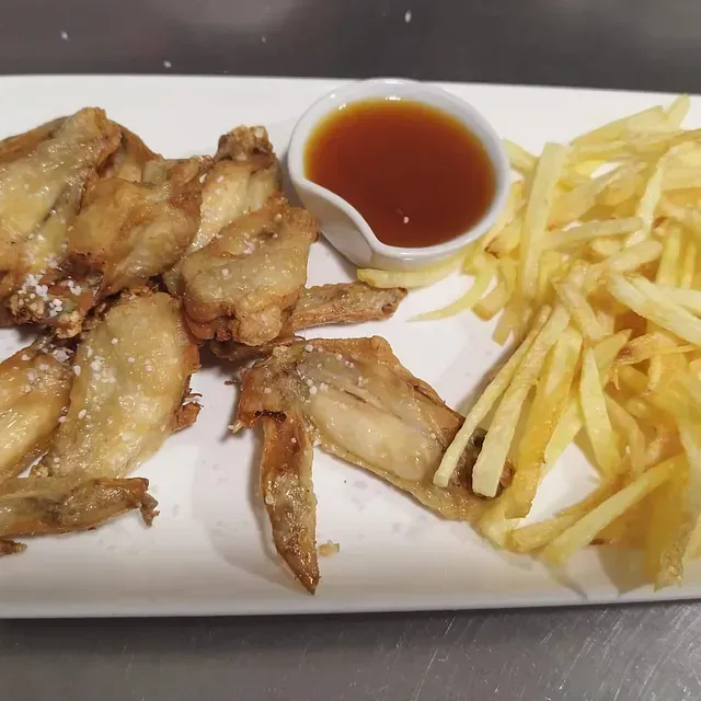 Un plato blanco cubierto con alitas de pollo y papas fritas.