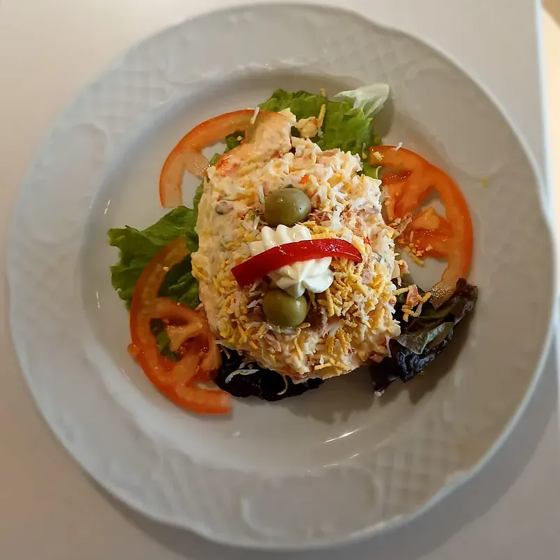 Un plato blanco cubierto con una ensalada con tomates y aceitunas.