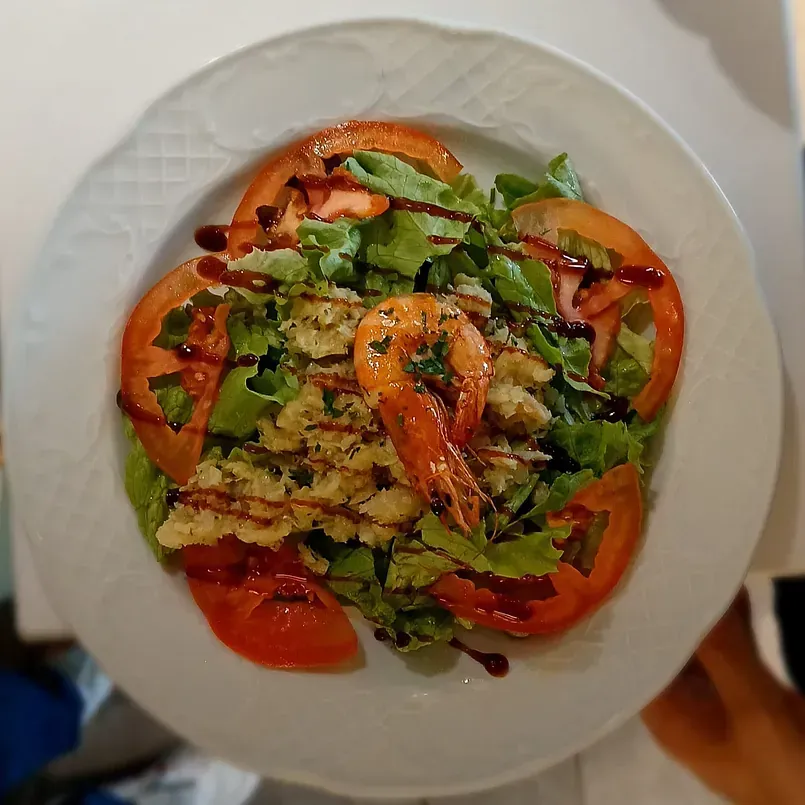 Una persona sostiene un plato de ensalada de camarones con tomates y lechuga.