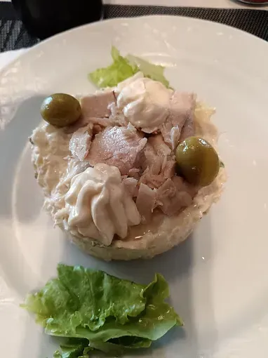 Un plato blanco cubierto con un pequeño sándwich con carne, aceitunas y lechuga.