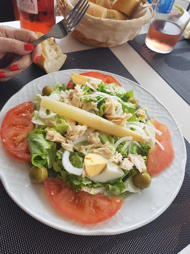 Un plato blanco cubierto con una ensalada con tomates, aceitunas, queso y atún.