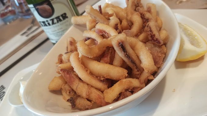 Un tazón de calamares fritos junto a una botella de Rizk