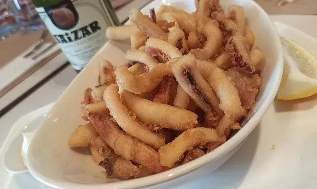 Un plato de calamares fritos junto a una botella de txazar